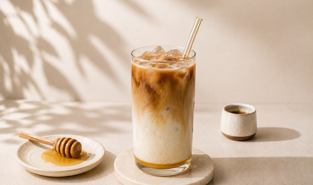Glas gefüllt mit äthiopischem Hong Latte und Eiswürfeln. Espresso Tasse und Honiglöffel im Hintergrund