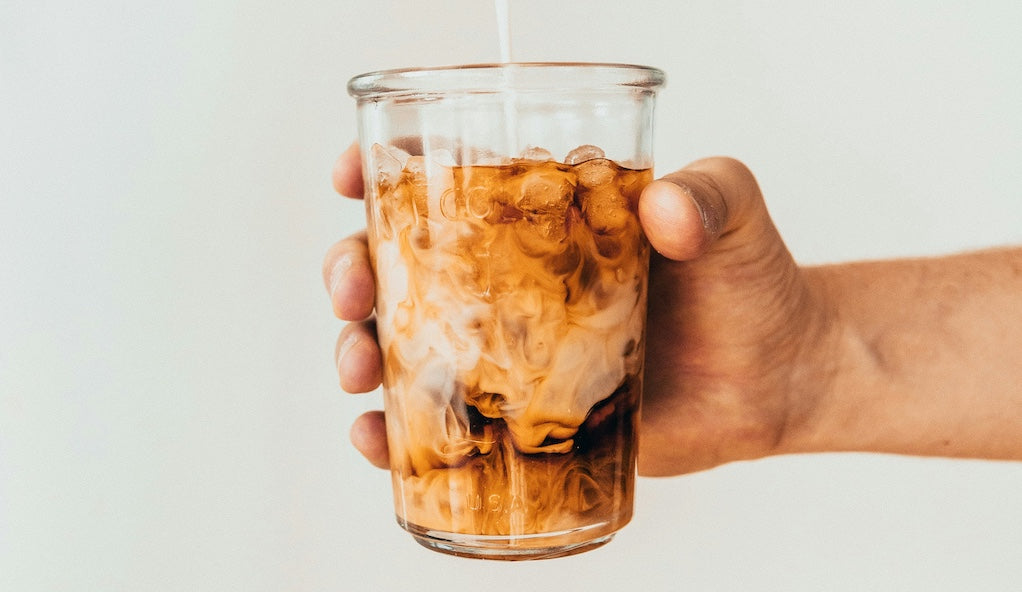 Hand hält Glas mit Cold Brew, Milch wird ins Glas gegossen