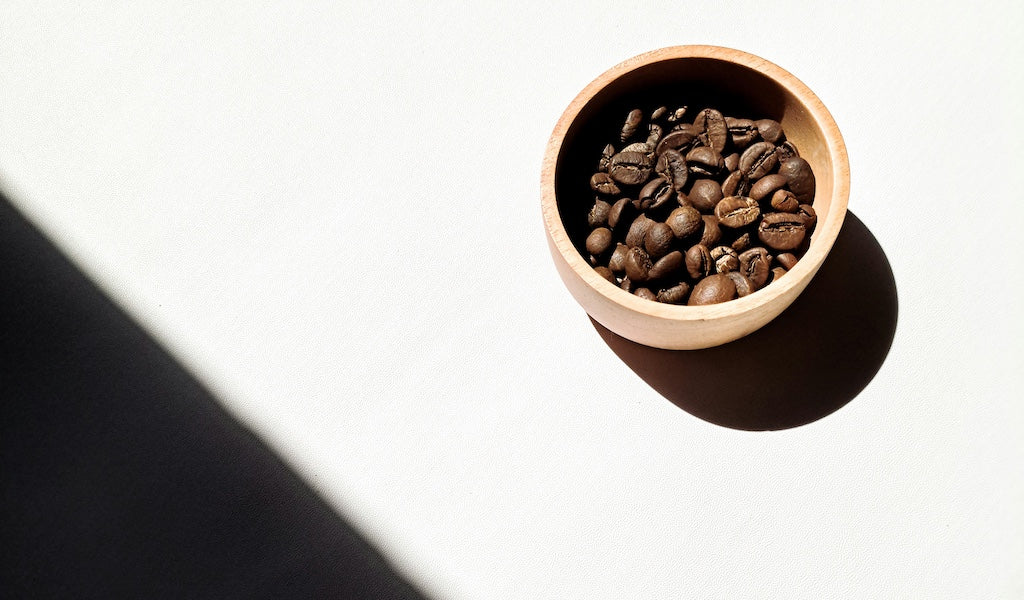 Schälchen mit ganzen Kaffeebohnen auf weißen Untergrund
