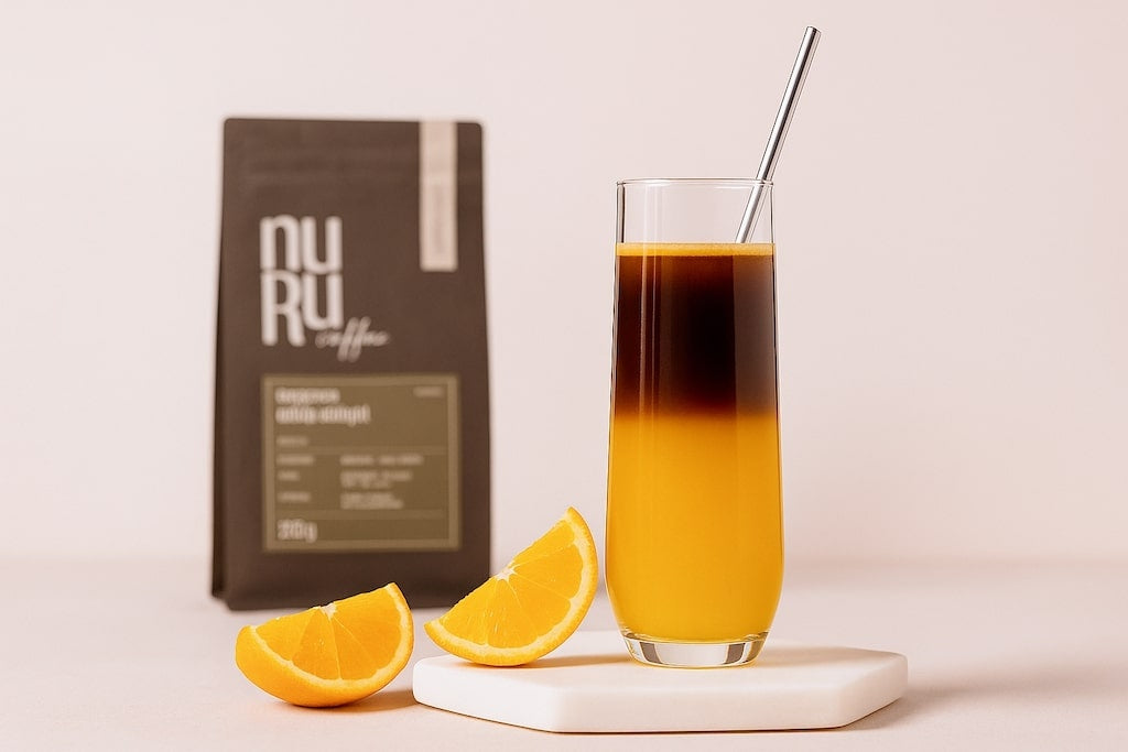 Espresso mit Orangensaft in hohem Glas mit Strohhalm, platziert auf weißer Platte mit Kaffeeverpackung im Hintergrund