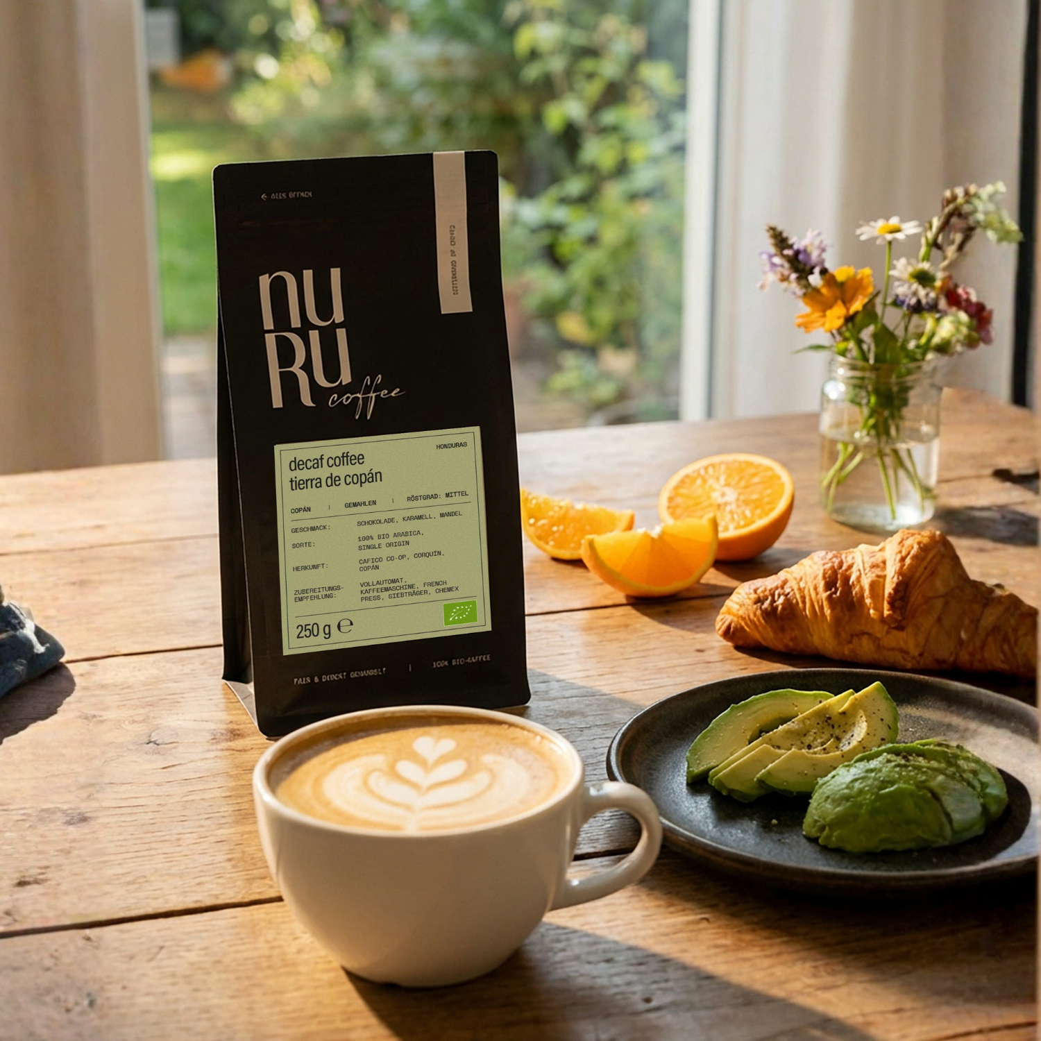 BIo entkoffeinierter Kaffee auf Frühstückstisch mit Avocado, Croissant, Orange und Wiesenblumen