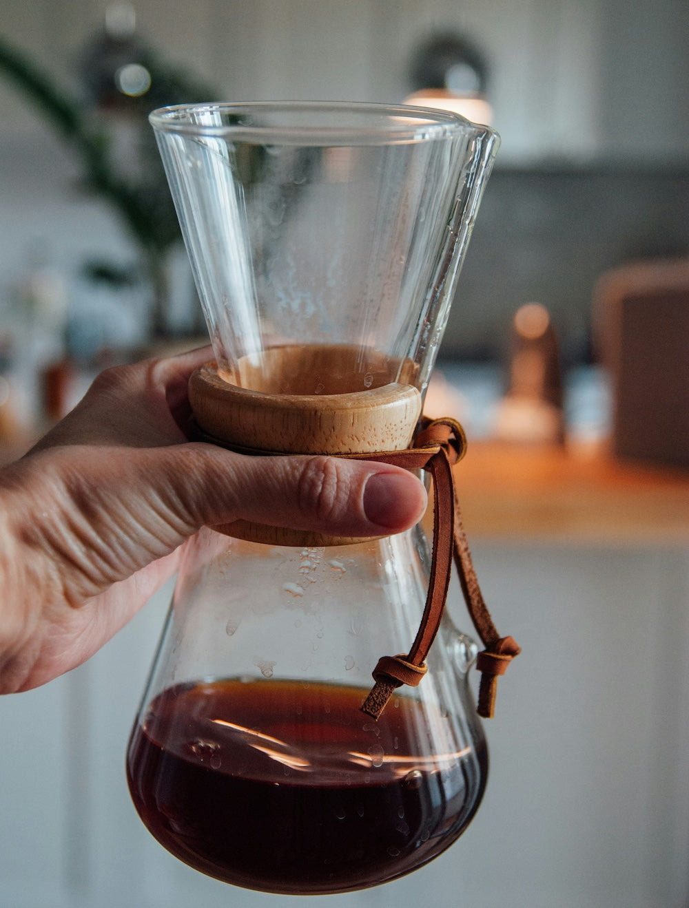 Hand hält Chemex Karaffe für 2 Tassen, verschwommene Küche im Hintergrund