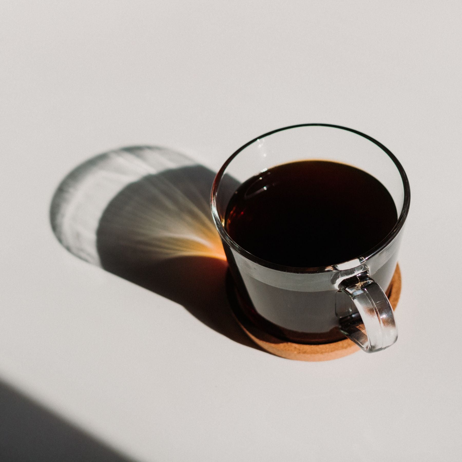 Glastasse mit schwarzem Kaffee gefüllt auf weißem Hintergrund mit Schatten