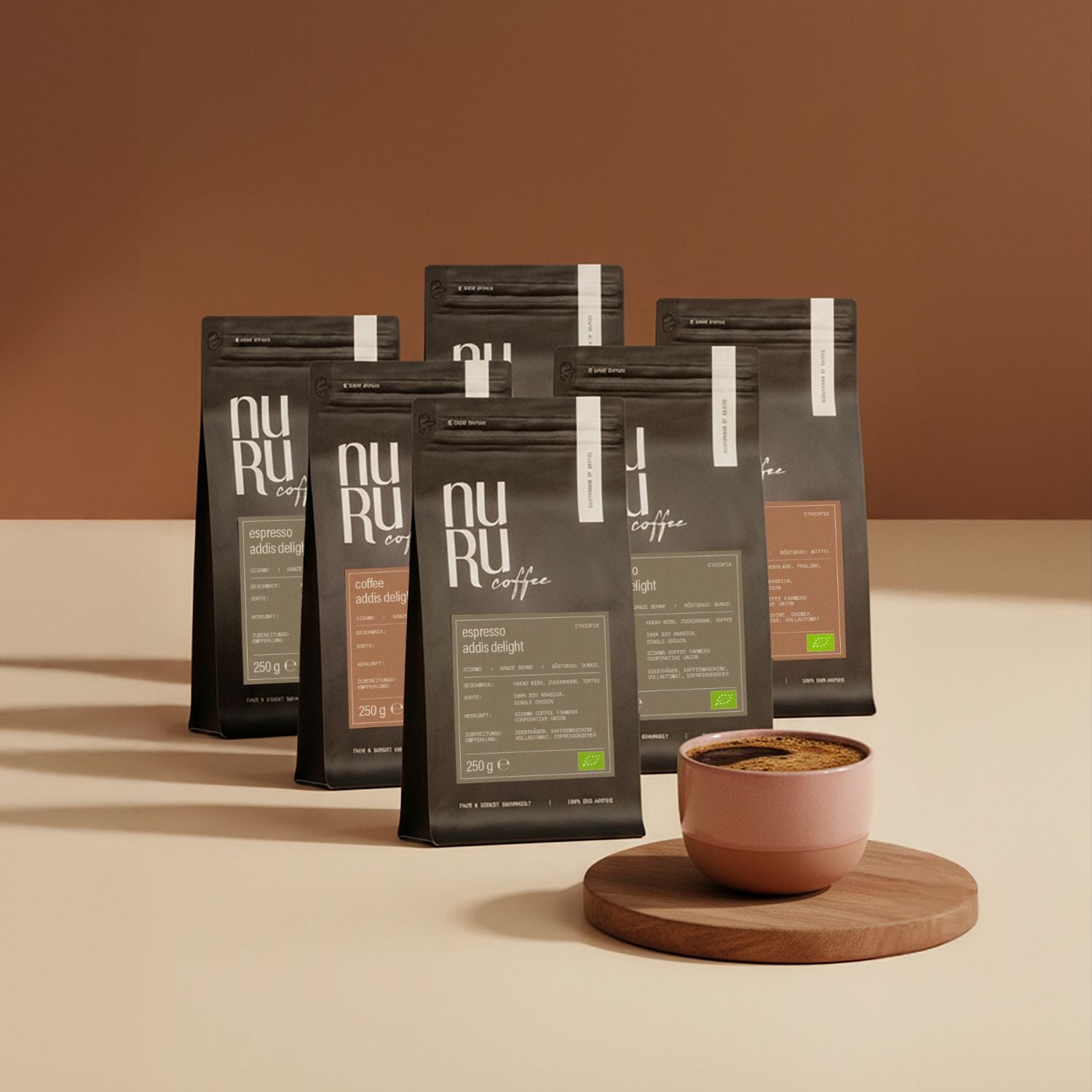 6 Packungen nuruCoffee auf cremefarbigem Hintergrund, rosa Keramiktasse mit schwarzem Kaffee auf Holzbrett